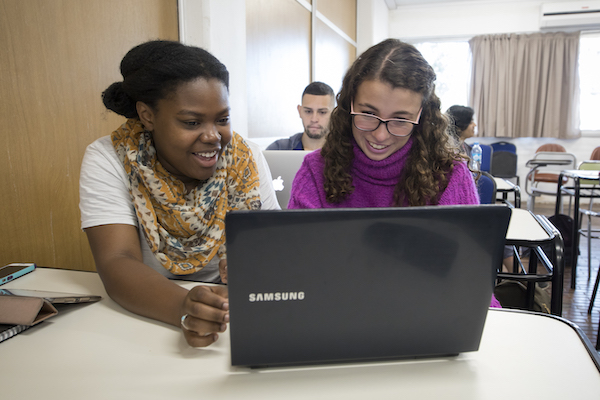 Photo that shows two people sitting side-by-side, smiling, and using a laptop together.